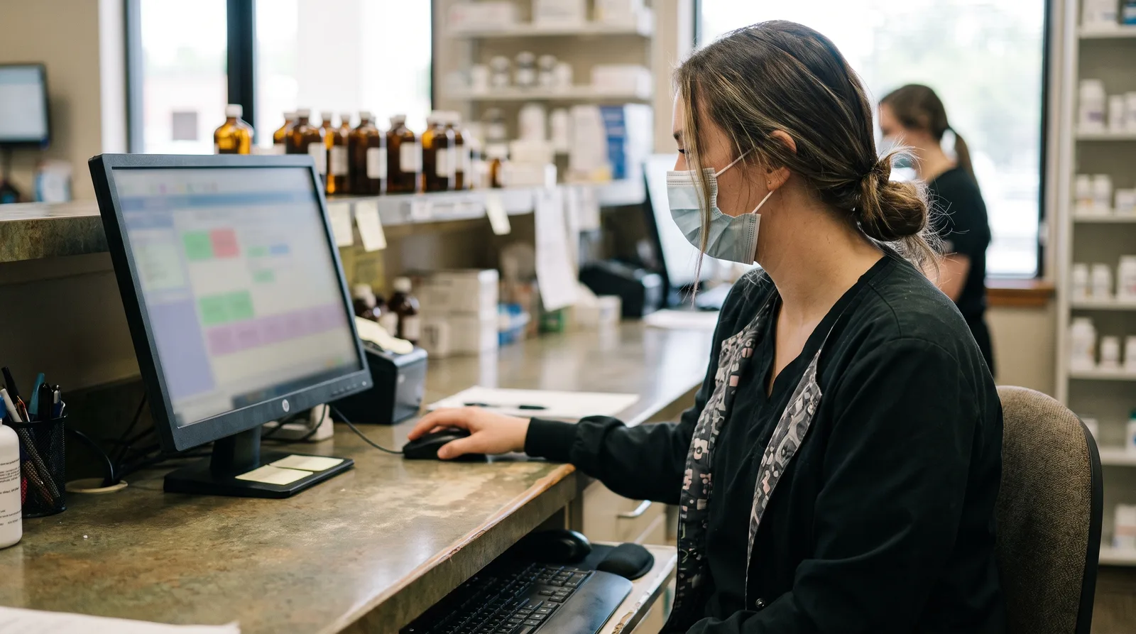 Pharmacist reviewing a secure HIPAA-compliant pharmacy website intake form on a computer at the counter